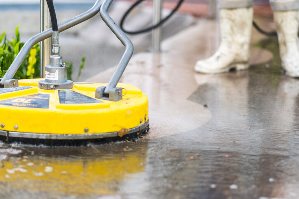 A worker using industrial equipment to perform pressure washing services on a sidewalk.
