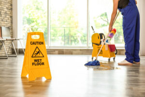 A yellow “CAUTION WET FLOOR” sign with a person mopping in the background in an office in El Paso.
