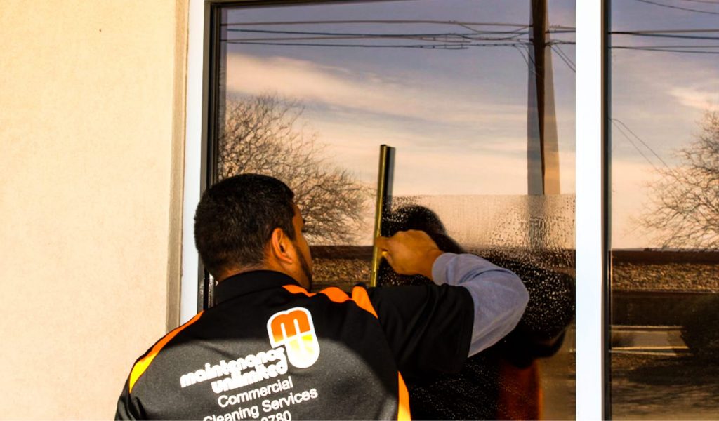 A Maintenance Unlimited window cleaning professional using a squeegee to clean a commercial building’s window.