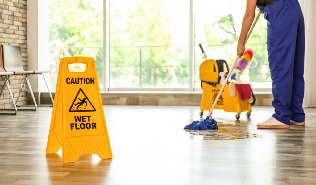 A yellow “CAUTION WET FLOOR” sign with a person mopping in the background in an office in El Paso.