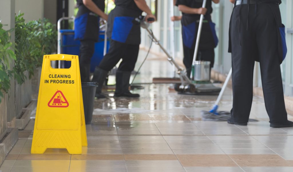 A team of professional cleaners cleaning the floors of an El Paso office space with a yellow sign on the ground reading “CLEANING IN PROGRESS.”