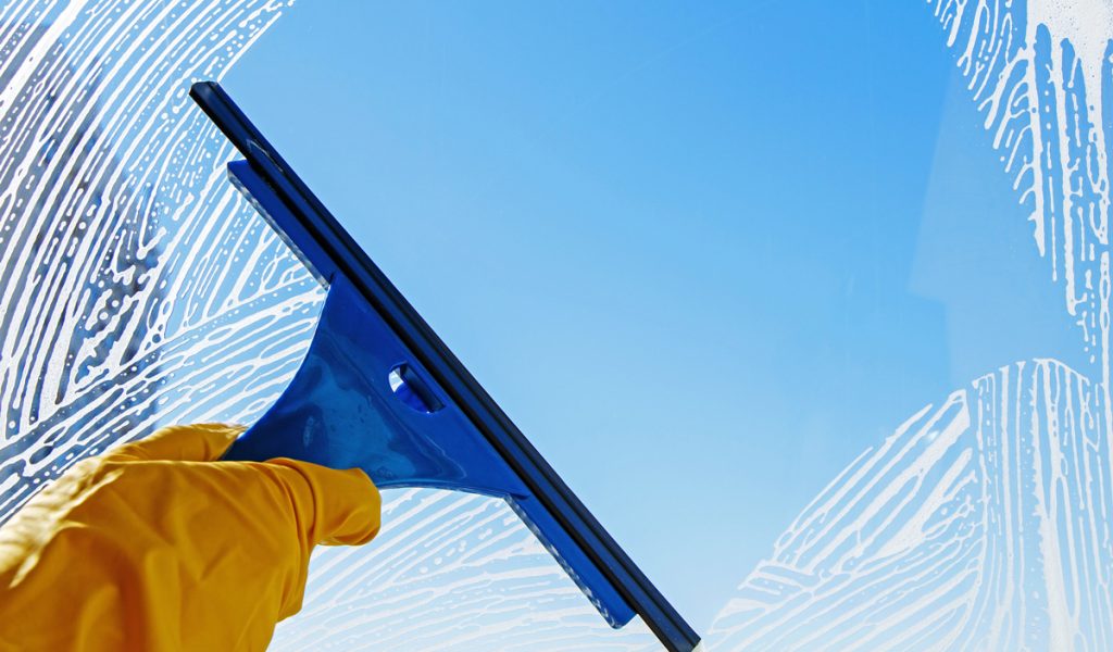 A person’s hand with a yellow glove wiping down a clean window in El Paso.