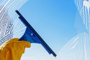 A person’s hand with a yellow glove wiping down a clean window in El Paso.